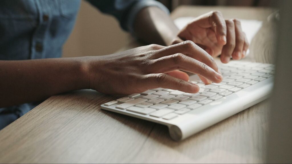 A dark-skinned woman types on a wireless keyboard.