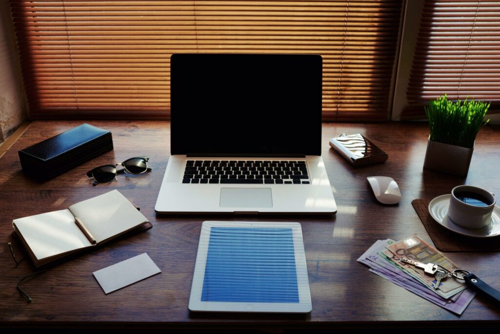A laptop sits open on a desk behind a large digital tablet. A cup of coffee, an open book, and other items sit on the desk, as well.