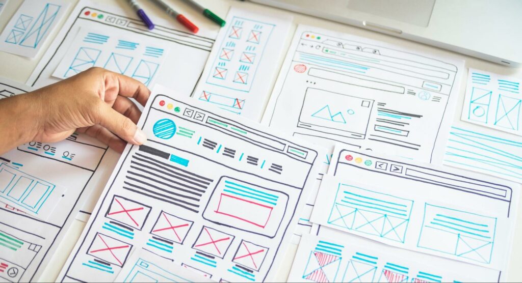 Several pieces of paper featuring color-coded wireframes of web pages are arranged on a table.