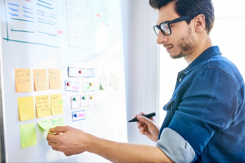 A man lays out sticky notes on a whiteboard to plan the design of an interface with user experience in mind.