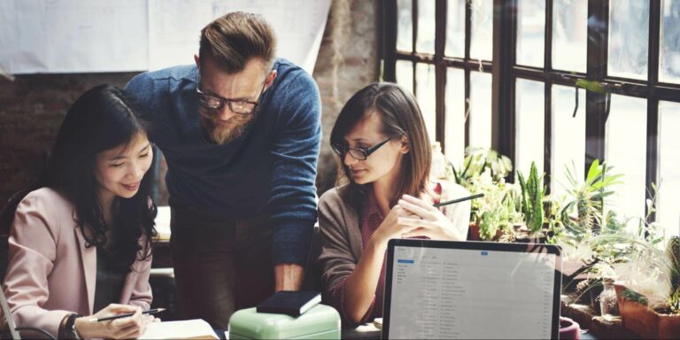 Three business bloggers gather around a notebook to discuss their blogging strategy.