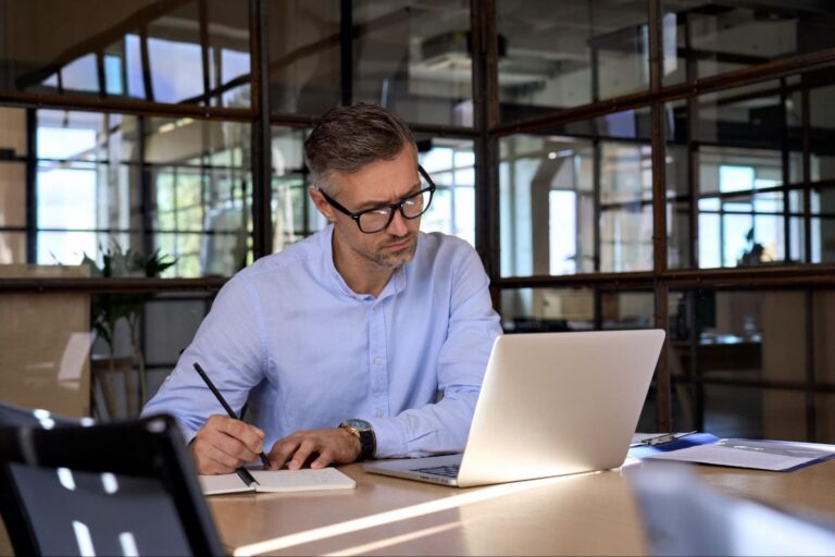 A man optimizing performance max campaigns on a laptop and writing notes.